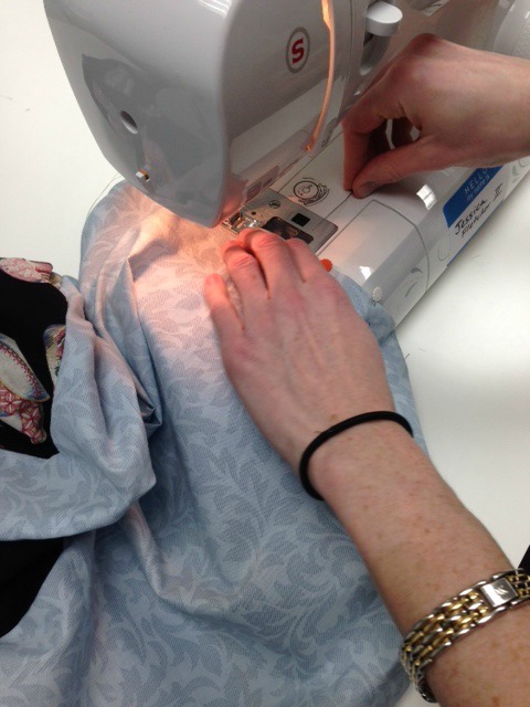 Image shows a close-up of a person sewing a blue floral fabric on a sewing machine.