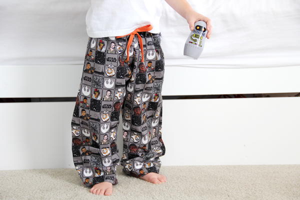 Image shows a close-up of a child standing in a room wearing the Saber the Moment DIY Pajamas and holding a Star Wars toy.