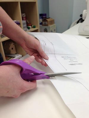 Image shows a person cutting out a paper template for a sewing project.