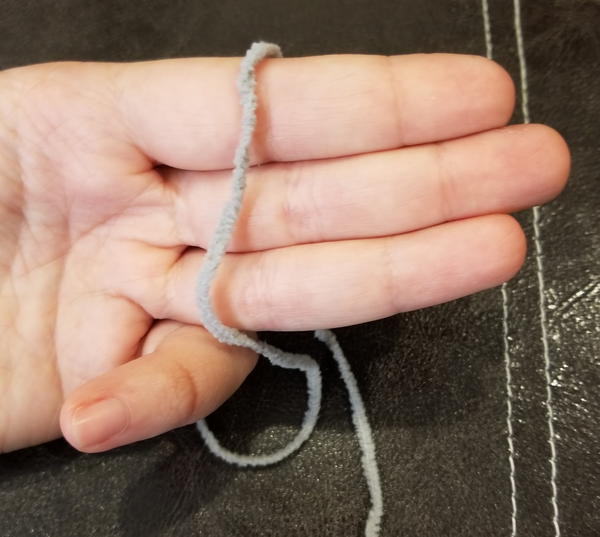 Image shows a hand with three fingers out and together holding a piece of yarn (step 1).
