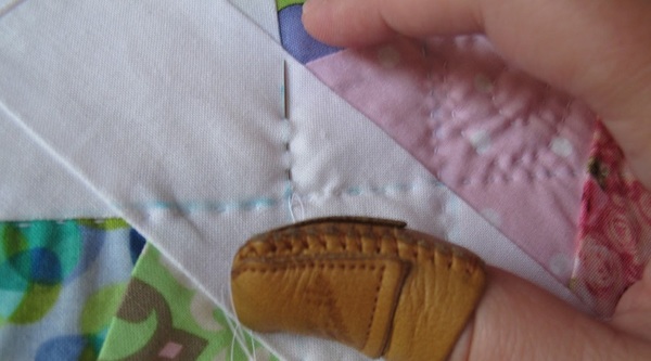 Basic Quilting by Hand: Image shows a close-up of a thimble-covered thumb pushing a needle through quilted fabric.