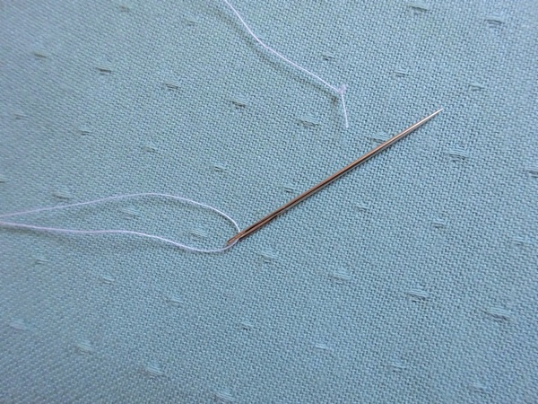 Image shows the hand sewing needle threaded and the end of the thread knotted.