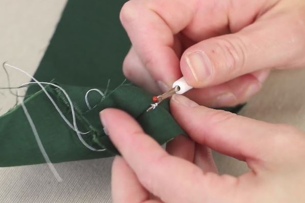 Images shows a close-up of a person using a seam ripper to remove a stitch from green fabric.