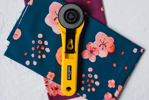 Image shows a light gray suface with two stacks of floral fabric. On top sits a yellow-handled rotary cutter.