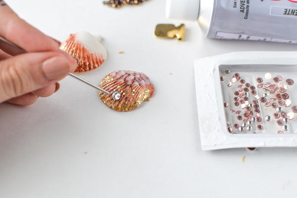 Using glue to adhere a rhinestone to a seashell.