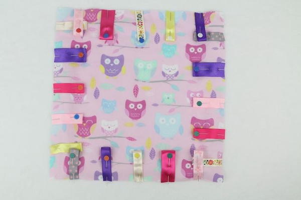 Image shows a square piece of fabric with folded ribbons arranged and pinned around all four sides.