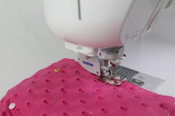 Image shows a sewing machine sewing the fabric pieces together.