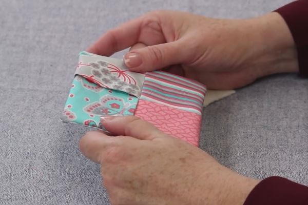 Image shows hands holding the sewn folded fabric coaster on a gray background.