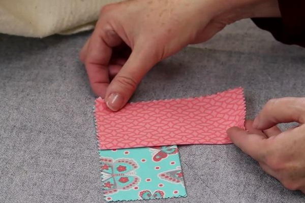 Image shows hands arranging two rectangle fabric pieces to make the square folded fabric coaster on a gray background.