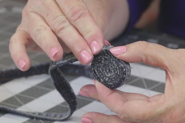 Image shows a cutting mat background with a hand holding and pressing down the rolled jean coaster in progress.