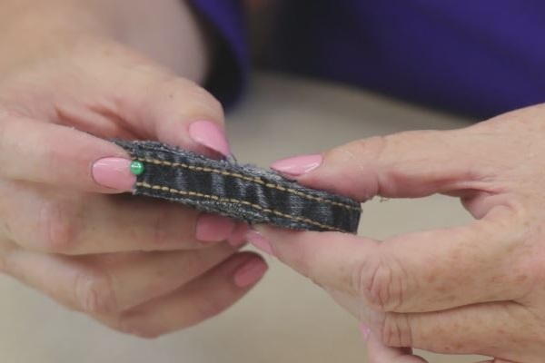 Image shows two hands holding the finished rolled jean coaster with a pin pushed down on the end piece.
