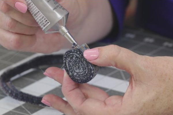 Image shows a cutting mat background with a hand holding and gluing the rolled jean coaster in progress.