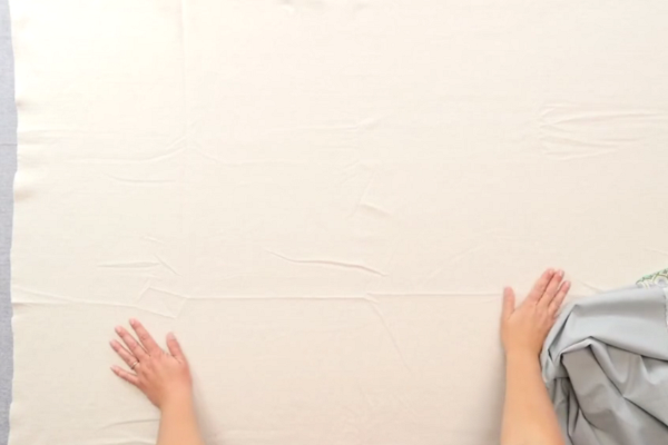 Image shows hands flattening a large piece of batting on a gray table.