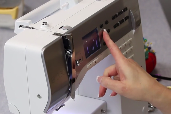 Image shows a close-up of someone choosing a stitch on a sewing machine.