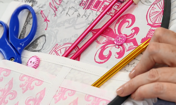 Image shows close-up of the embroidery hoop organizer pockets with scissors and knitting needles inside.