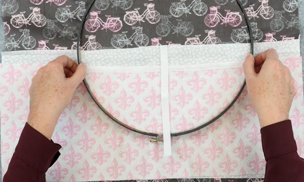 Image shows hands adjusting the outer embroidery hoop over another set of fabric pieces (the pockets).