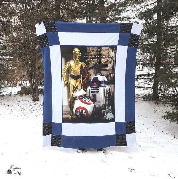 Image shows a person standing in a snowy yard holding up the Star Wars-Inspired Reversible Fleece Quilt.