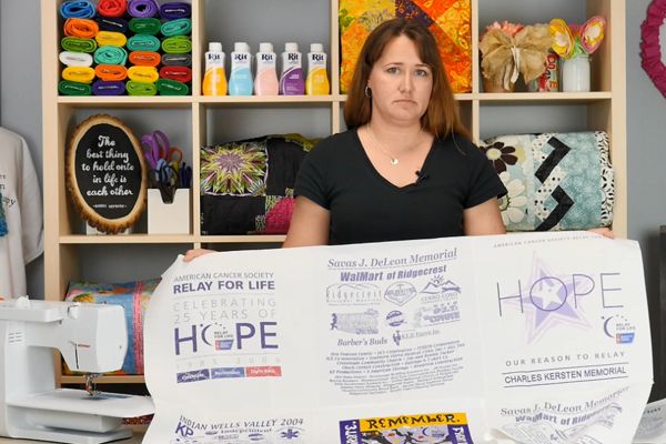 Image shows Carolina holding up the sewn quilt in a craft room.