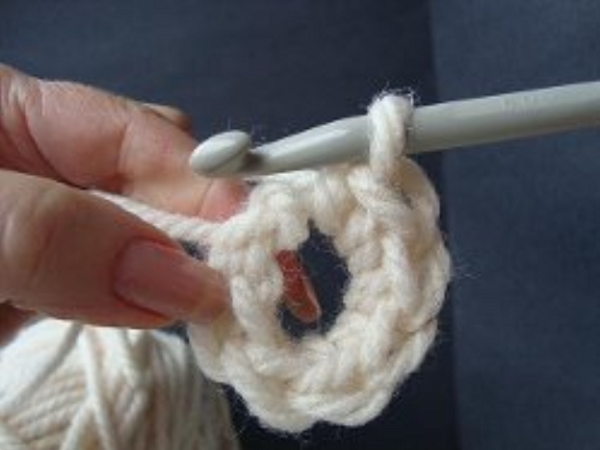 Image shows step 9 for crocheting a magic ring, which shows a hand holding yarn. There's a hook in the other hand pulling the single crochet into the main loop.