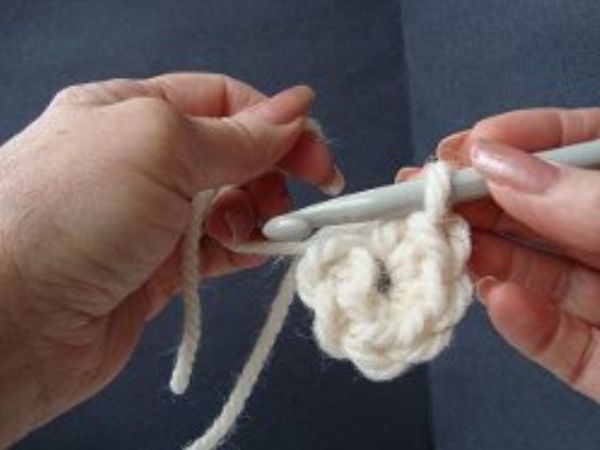Image shows step 10 for crocheting a magic ring, which shows a hand holding yarn. There's a hook in the other hand pulling the single crochet into the main loop.