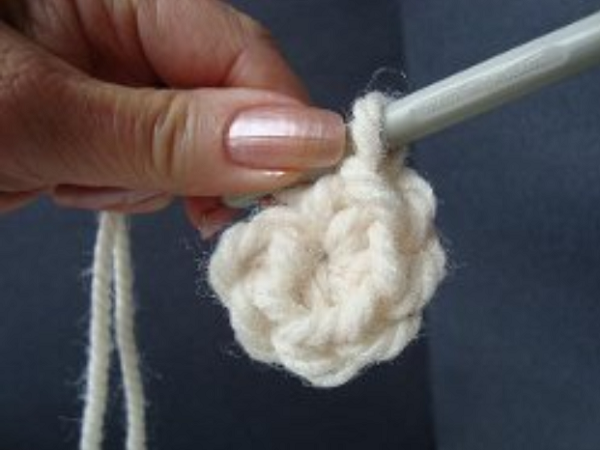 Image shows step 11 for crocheting a magic ring, which shows a hand holding yarn. There's a hook in the other hand with the finished crochet magic circle.