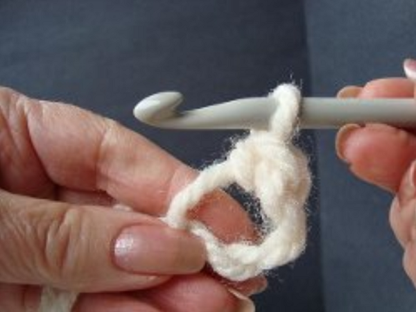 Image shows step 8 for crocheting a magic ring, which shows a hand holding yarn. There's a hook in the other hand pulling the yarn through to make a single crochet stitch.