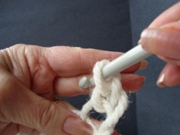 Image shows step 5 for crocheting a magic ring, which shows a hand holding yarn in a loop. There's a hook in the other hand pulling the yarn through to make a chain stitch.
