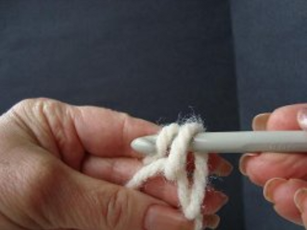 Image shows step 4 for crocheting a magic ring, which shows a hand holding yarn. There's a hook in the other hand pulling the yarn through to make a chain stitch.