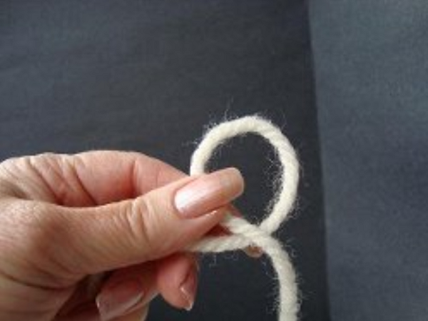Image shows step 1 for crocheting a magic ring, which shows a hand holding yarn in a loop.