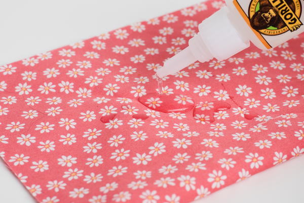 Image shows super glue being applied to a piece of patterned fabric.