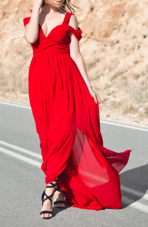 Image shows a woman wearing a draped long formal red dress on a street.