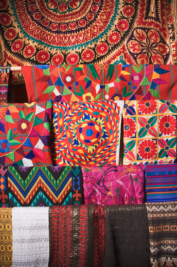 Image shows a display of various and vibrant folded quilts.