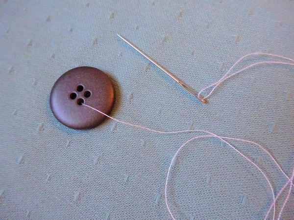 Image shows the button on fabric with the thread through one hole.