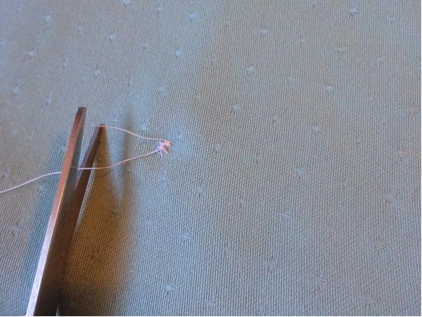 Image shows the back of the sewn button attached to the fabric. Scissors are cutting the excess thread after it has been knotted.