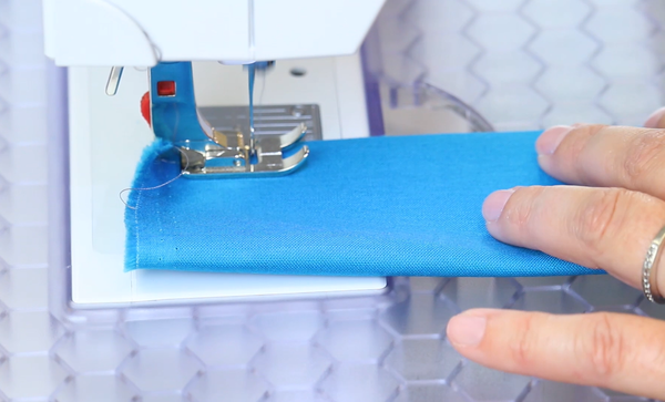 Image shows close up of a sewing machine sewing the blue fabric roll of the DIY tote bag.