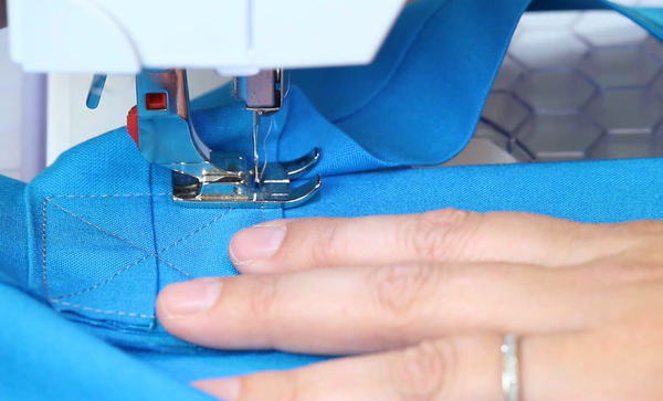 Image shows close up of a sewing machine sewing the blue fabric handles of the DIY grocery bag.