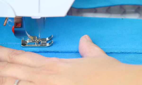 Image shows close up of a sewing machine sewing a line of stitching to secure the fold at the top of the bag.