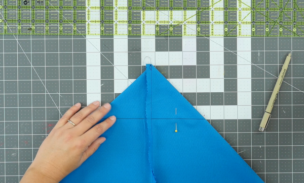 Image shows a cutting mat in the background. The sewn blue bag piece is being pinned.