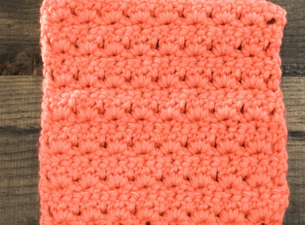 Image shows an orangish-pink yarn swatch made using the primrose stitch.