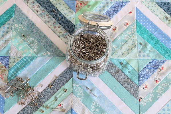 Sewing Inspiration - image shows safety pins on a quilted fabric background.