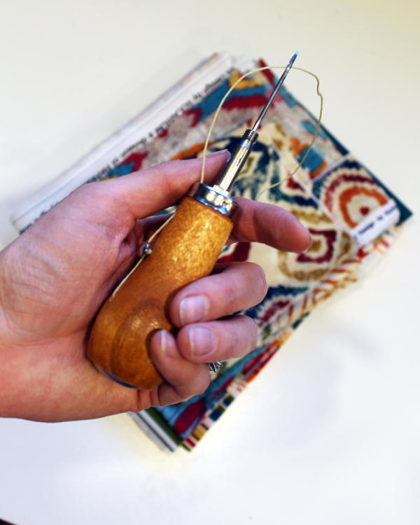 Example of canvas and person holding a sewing awl.
