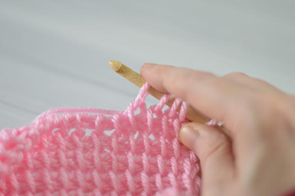Image shows a hand holding a Tunisian crochet hook that's pulling up a loop while crocheting.