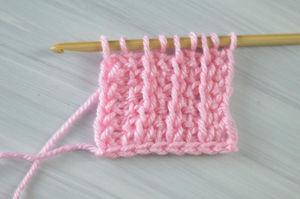 Image shows an example of pink yarn on a Tunisian crochet hook that features the simple ribbing technique.