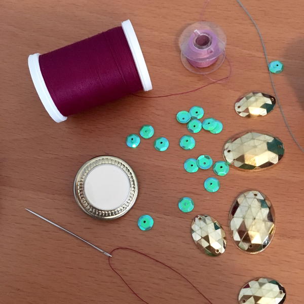 Image shows a variety of sewing notions and embellishments: thread, buttons, sequins, and a threaded needle.