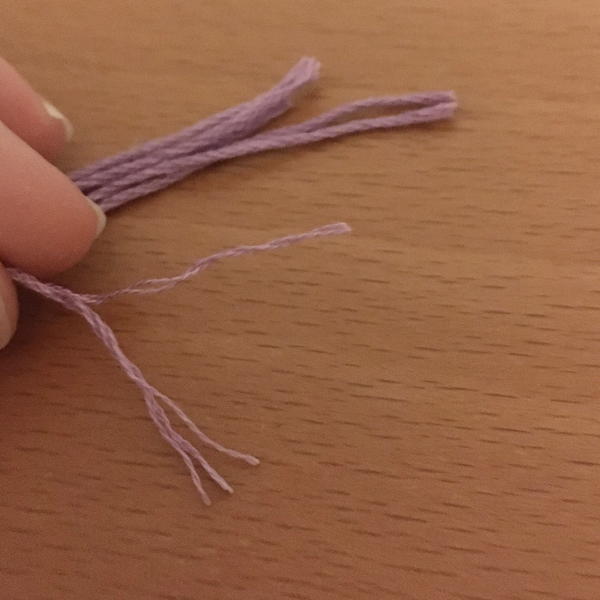 Image shows four full pieces of pink embroidery thread with one being pulled apart to reveal thinner strands on a wood surface.