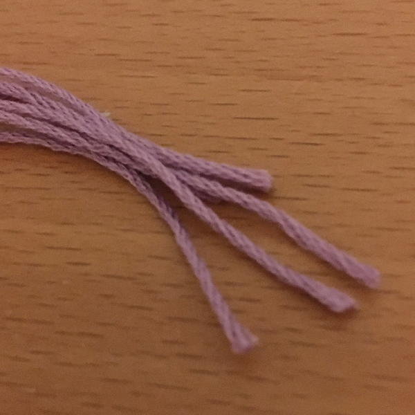 Image shows four full pieces of pink embroidery thread on a wood surface.