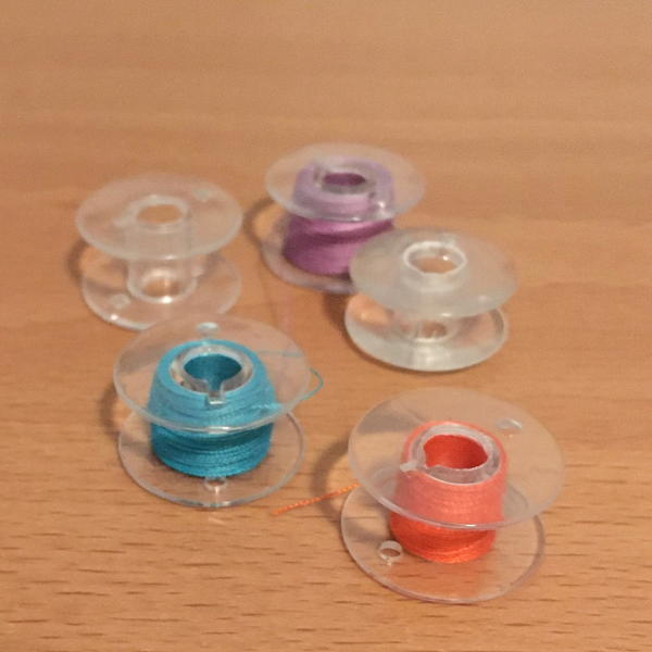 Image shows sewing machine thread bobbins with various-colored thread inside on a wood surface.