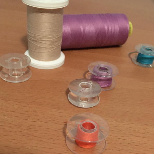 Image shows sewing machine thread bobbins and spools of thread on a wood surface.