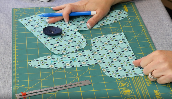 Image shows the two fabric pattern pieces, one with the button hole marked and one with the button sewn on.