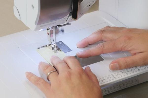 Image shows hands pushing fabric through a sewing machine.
